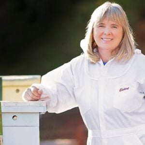 Master Beekeeper Charlotte Anderson wearing white bee suit inn apiary.