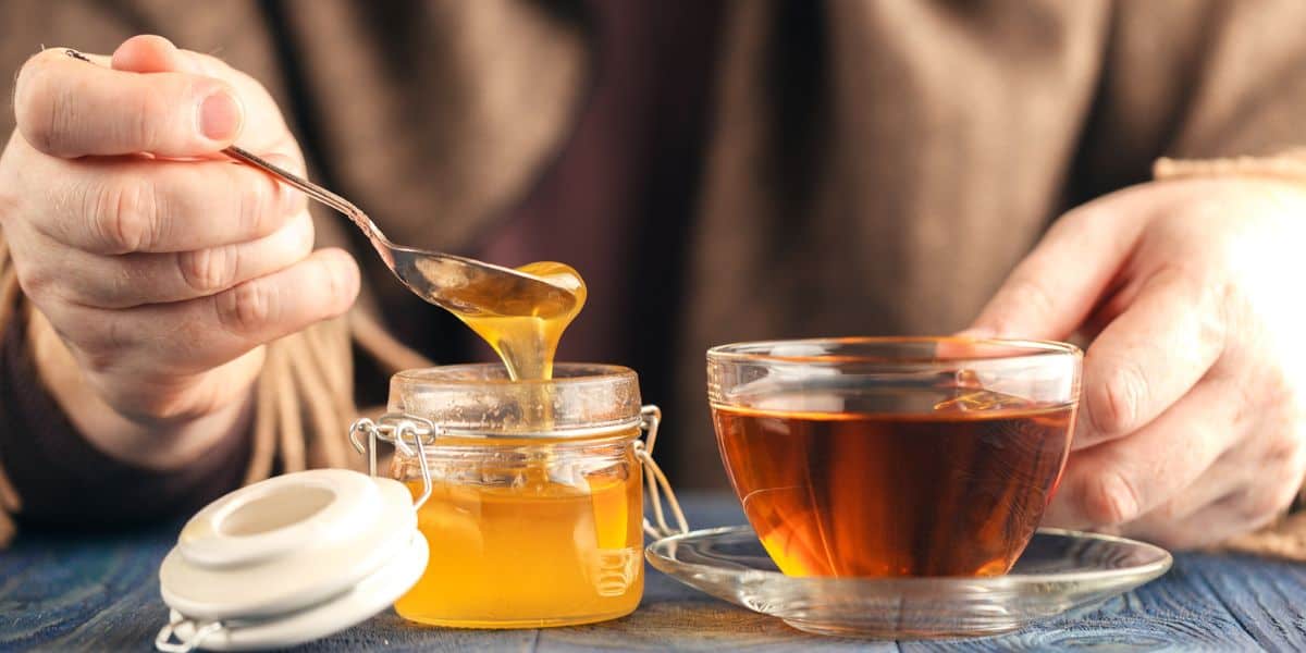 Tea pot with mug of hot tea and jar of honey.